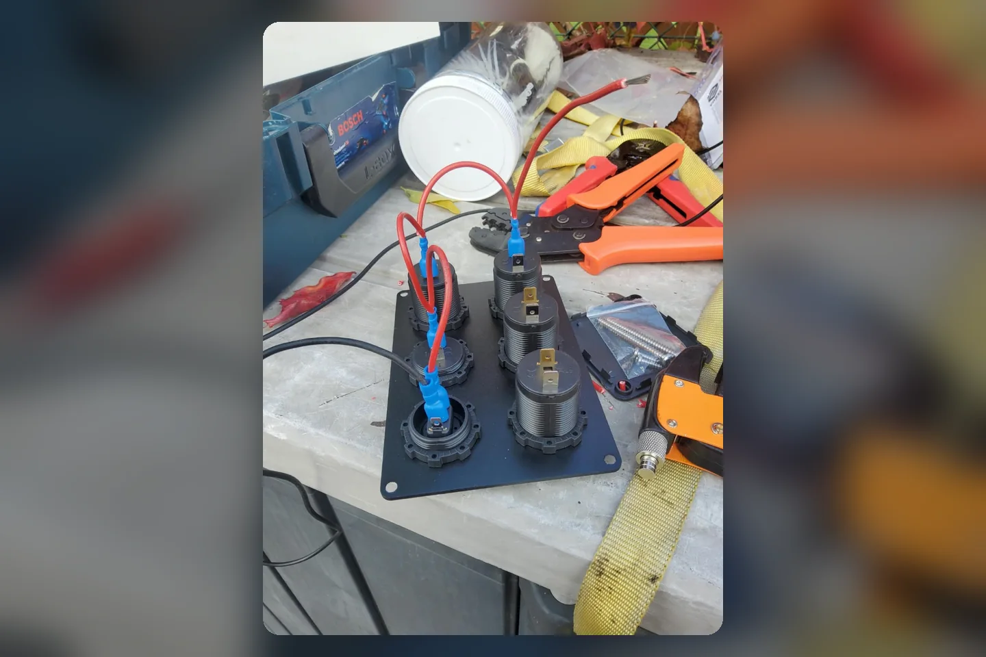 Mehrere runde 12-Volt-Anschlüsse mit roten Kabeln, Crimpzange und Werkzeug beim Ausbau der Camper-Elektrik