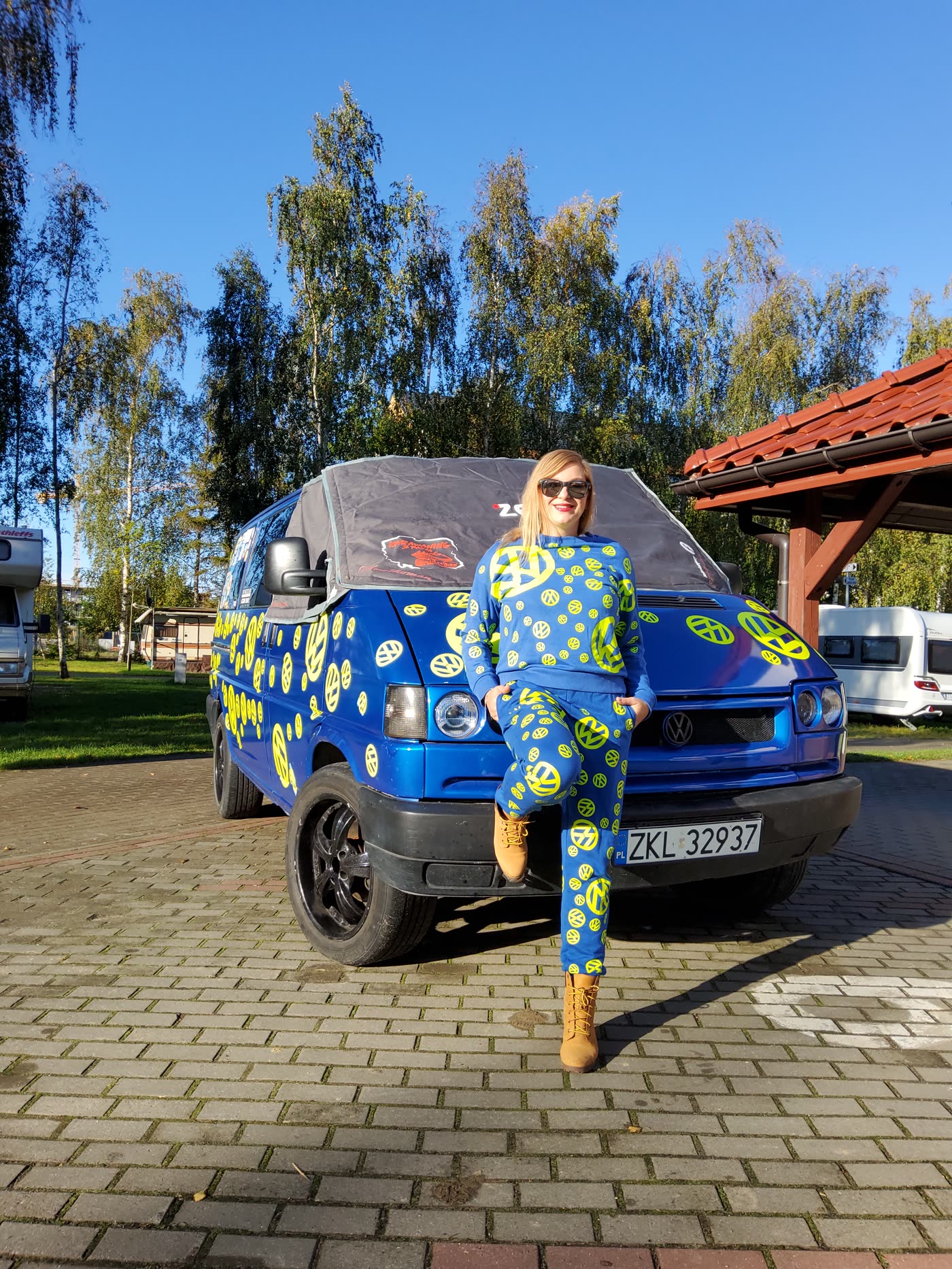 Tussy sitzt auf der Motorhaube ihres blauen VW T4 mit neongelben Stickern
